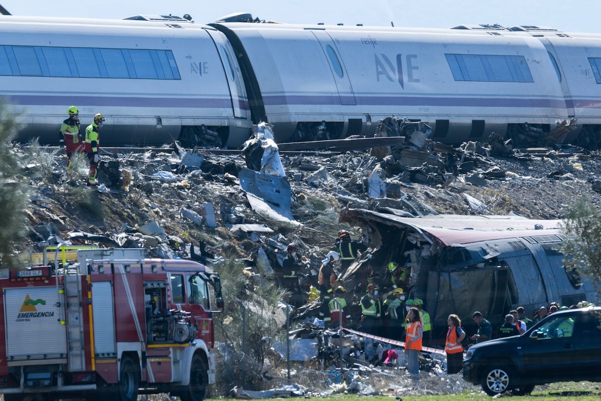 Vagões de um trem AVE descarrilados e destroços ao lado da via, com bombeiros e um caminhão de emergência em primeiro plano