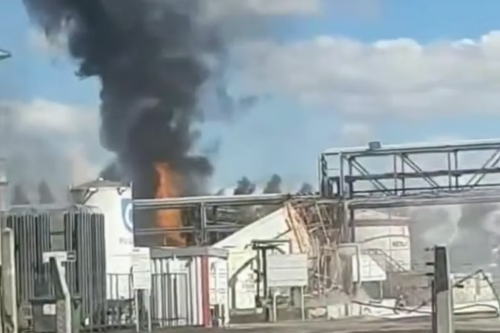 Coluna de fumaça preta e chamas entre tanques e estruturas metálicas de uma usina industrial