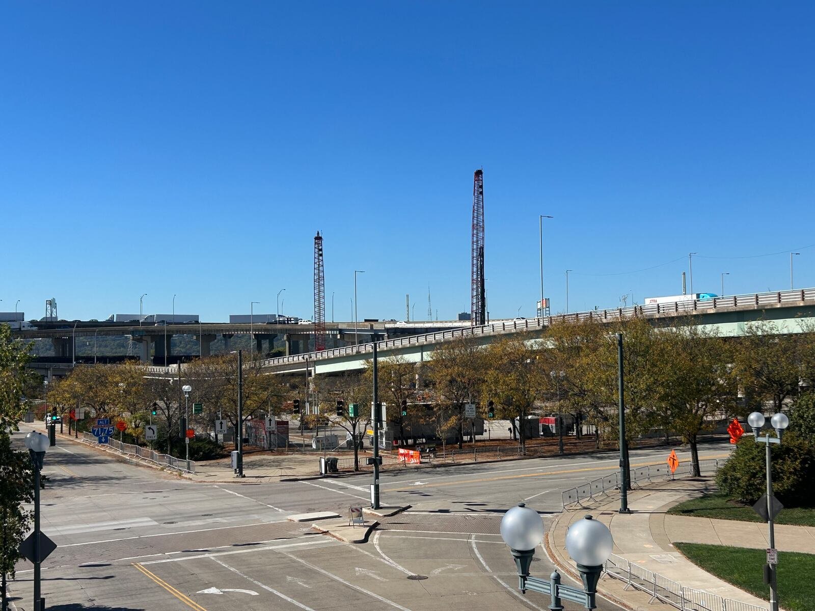 Cruzamento no centro de Cincinnati com viadutos da rodovia ao fundo e dois guindastes treliçados vermelhos no canteiro de obras