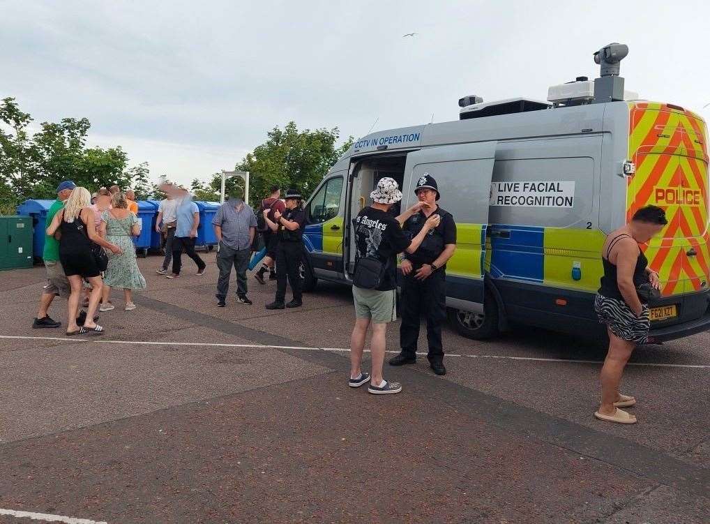 Van da polícia com câmeras no teto e o aviso "Live Facial Recognition" (reconhecimento facial ao vivo) estacionada num pátio em Lowestoft, com policiais conversando com o público