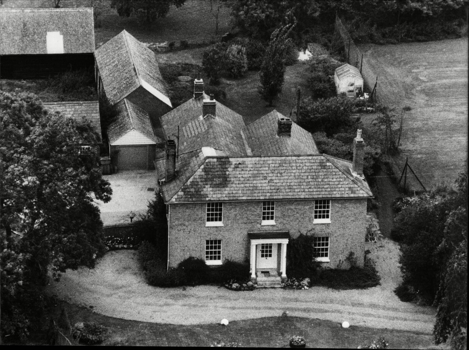 Foto aérea em preto e branco da casa da White House Farm, em Essex, com telhados, árvores e o caminho de entrada